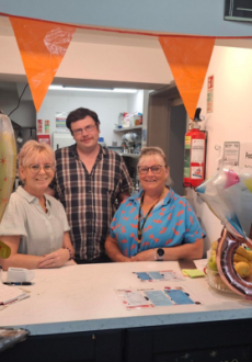 Two women and a man behind a kitchen counter in a cafe smiling