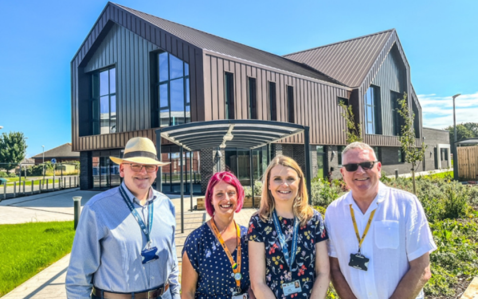 Two men and two women stood in front of a new large building in the sunshine