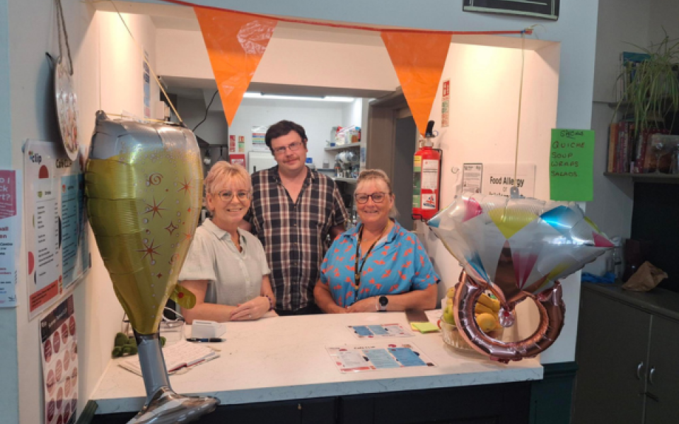 Two women and a man behind a kitchen counter in a cafe smiling