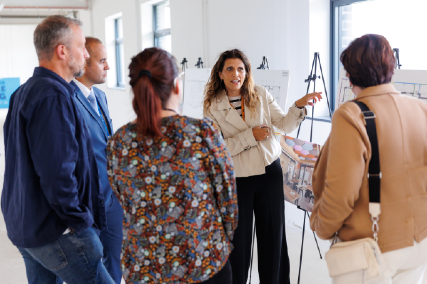 A woman talking to a group of people whilst pointing at a board