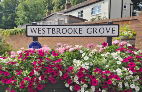 A photo of the street sign for Westbrooke Grove with flowers underneath