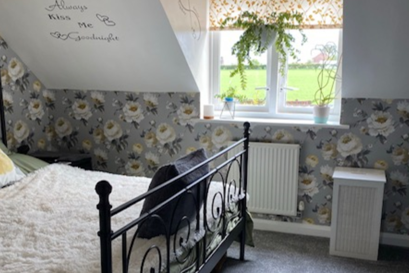 A photo of the bedroom showing a bed, wallpaper and windows