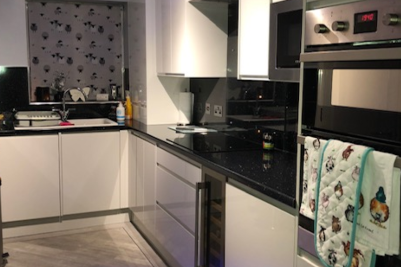 A photo of the kitchen with a white door, white cupboards and a black worktop