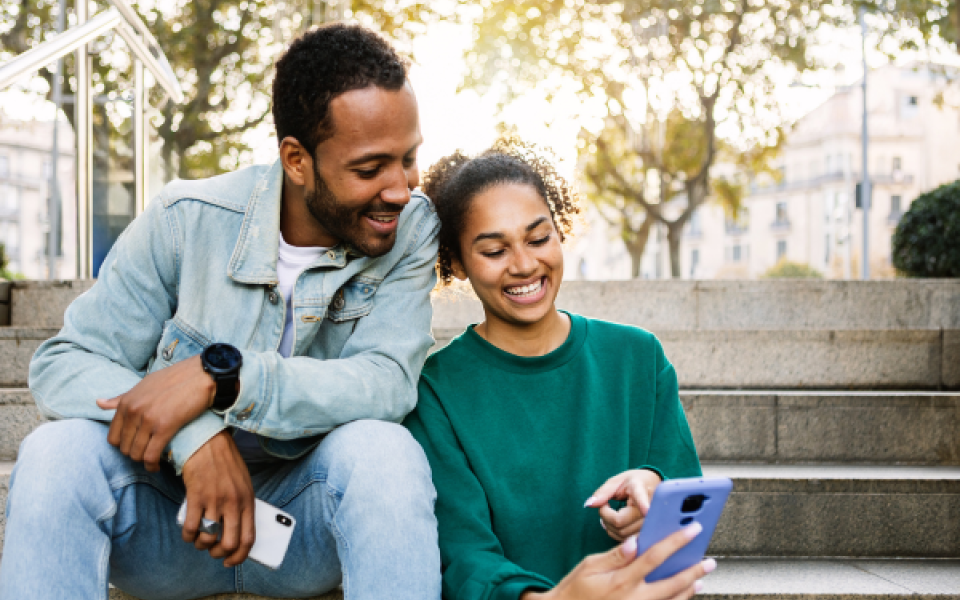 Two people sat on some steps looking at a phone and smiling