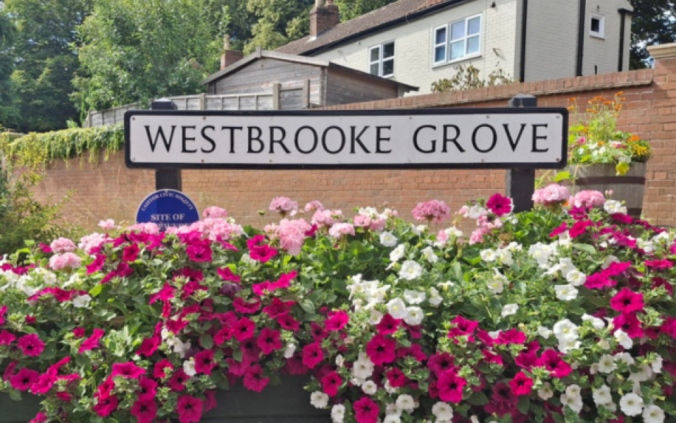 A photo of the street sign for Westbrooke Grove with flowers underneath